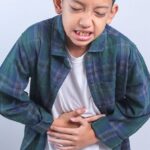 Child holding stomach in pain indicating possible gastrointestinal discomfort.