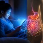 Professional using a smartphone and laptop late at night while experiencing bloating and digestive discomfort caused by excessive screen time and blue light exposure.